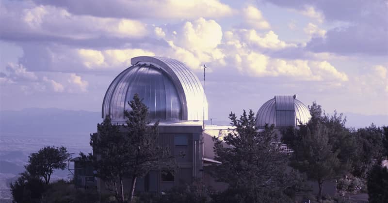 A silver observatory dome on a mountain ridge above the trees