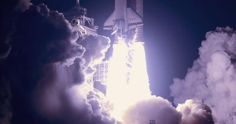 A space shuttle climbing into a night sky on a column of fire and steam, 1999