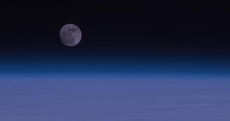The moon rising over the blue edge of Earth's atmosphere, photographed from orbit